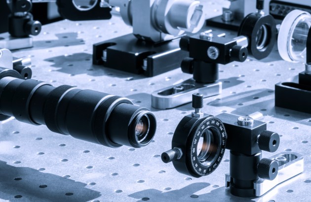 Optik- Optische Geräte, darunter ein Teleskop und Linsen, sind auf einem Tisch in einem Labor ausgestellt. Wissenschaftliches Experiment zum Thema Optik und Photonik mit Laserhintergrund