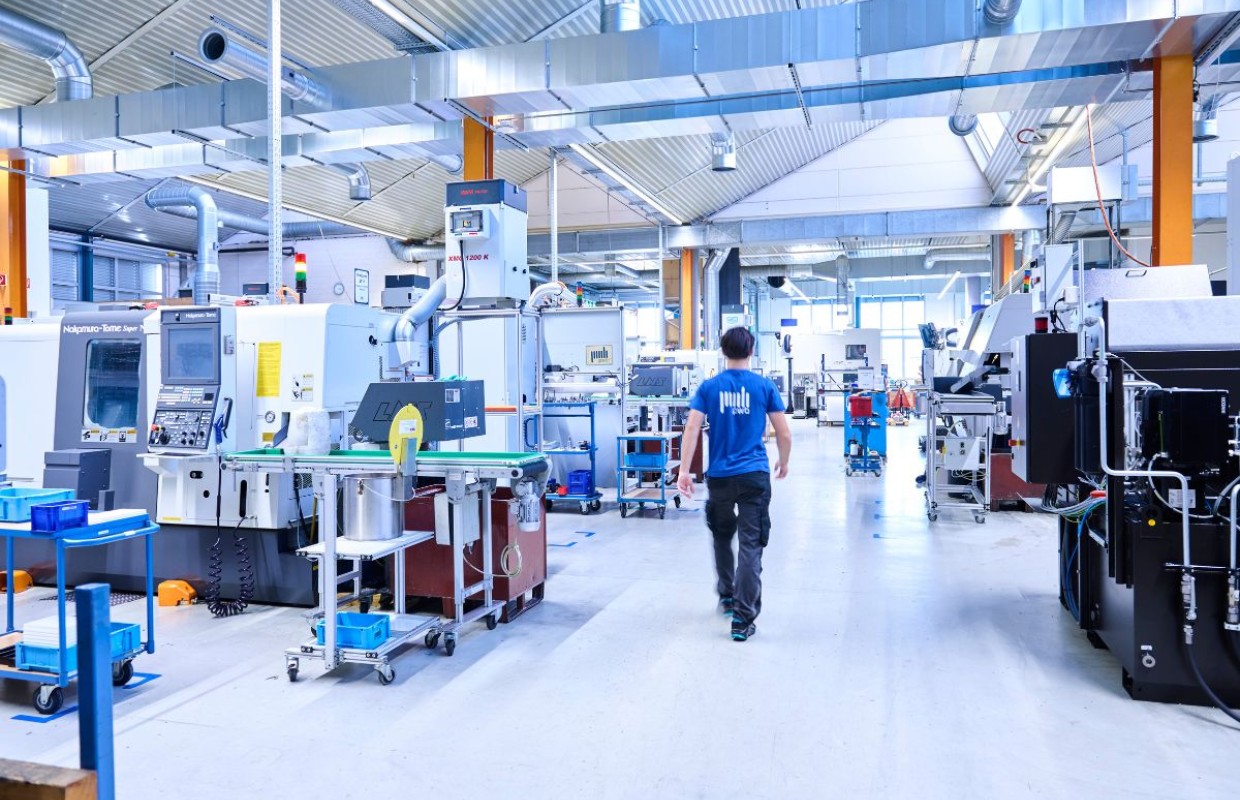 Mann läuft durch eine Produktionshalle mit Maschinen der CNC Fertigung auf ein Fenster zu