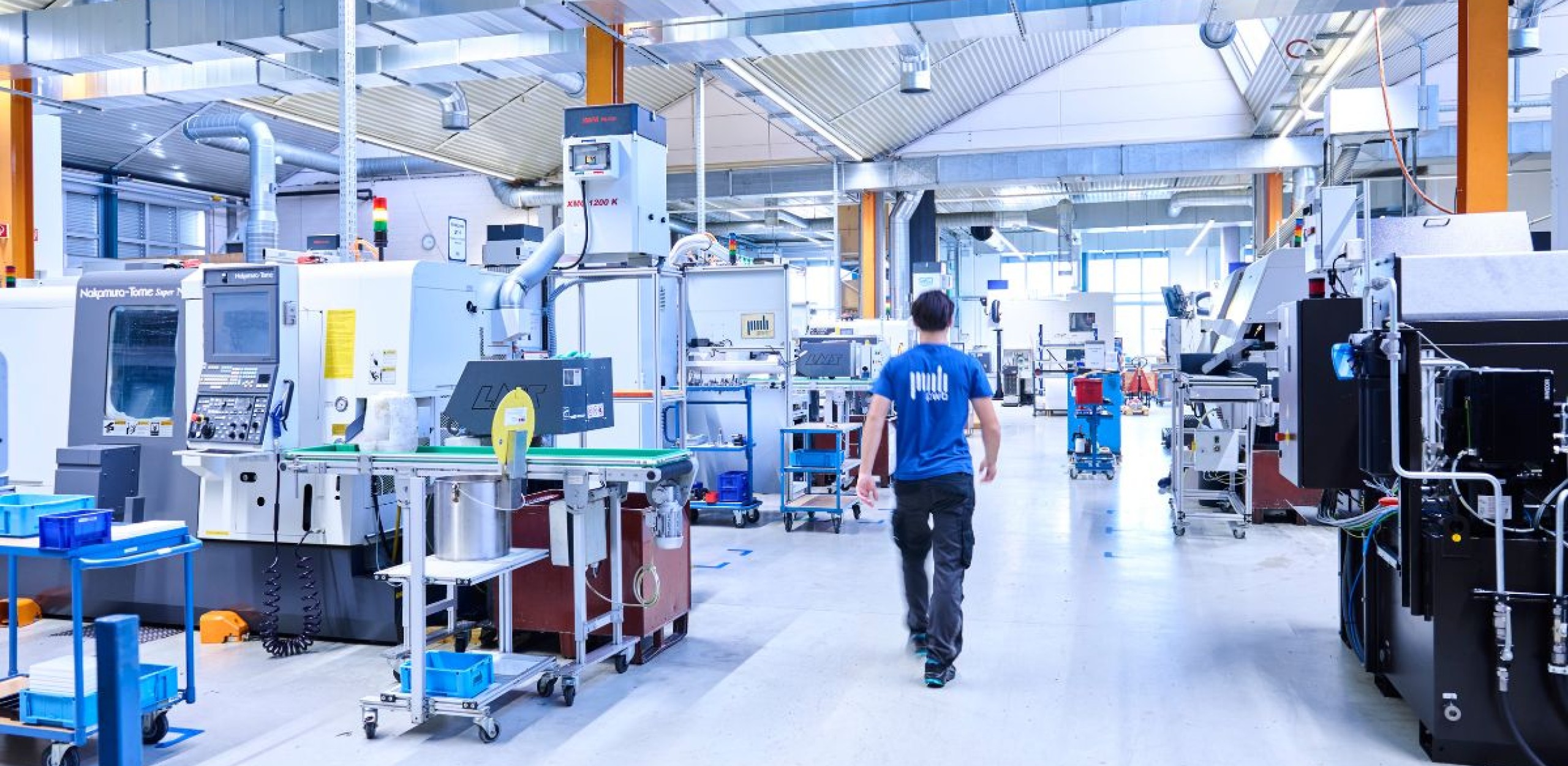 Mann läuft durch eine Produktionshalle mit Maschinen der CNC Fertigung auf ein Fenster zu