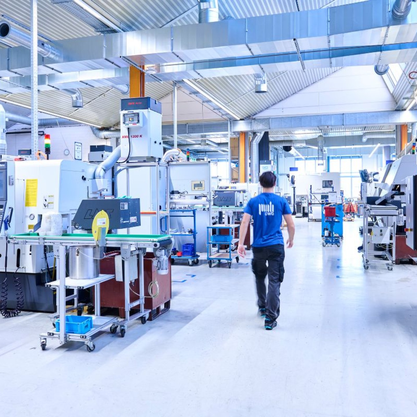 Mann läuft durch eine Produktionshalle mit Maschinen der CNC Fertigung auf ein Fenster zu