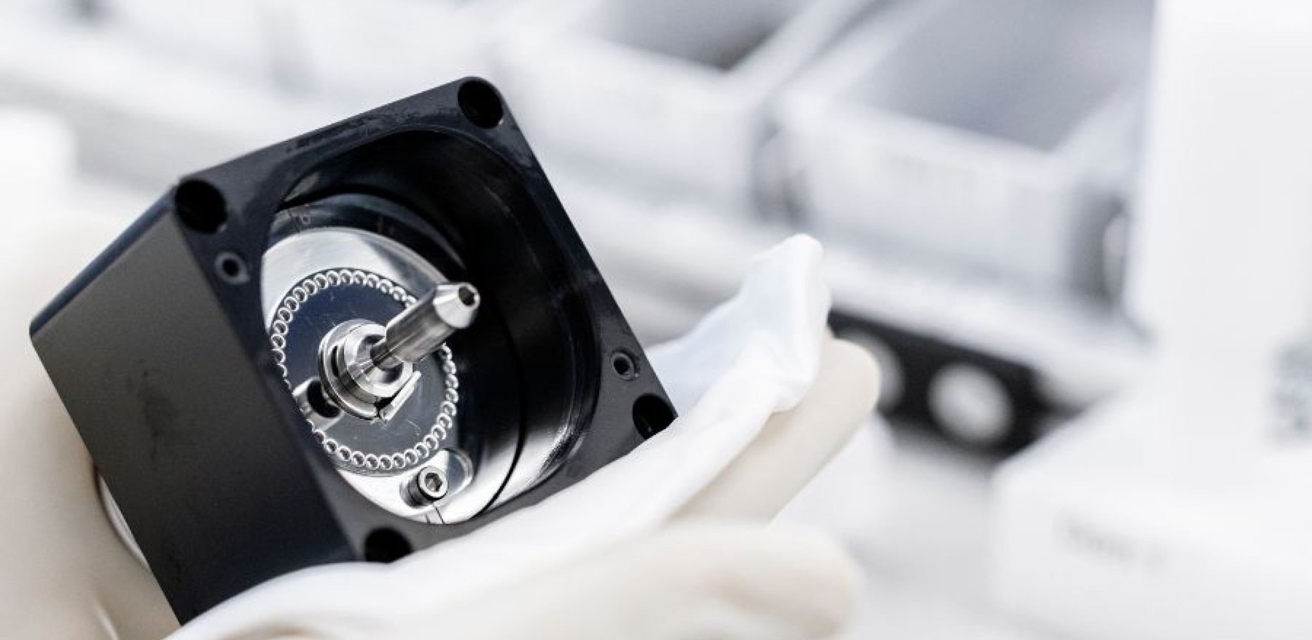 Zwei Hände in weissen Handschuhen halte ein Bauteil hoch und säubern es mit einem weissen Tuch